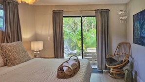 Ein Schlafzimmer mit Bett, einem Korbwäscheschrank, einem Stuhl und Blick auf Grünflächen.
