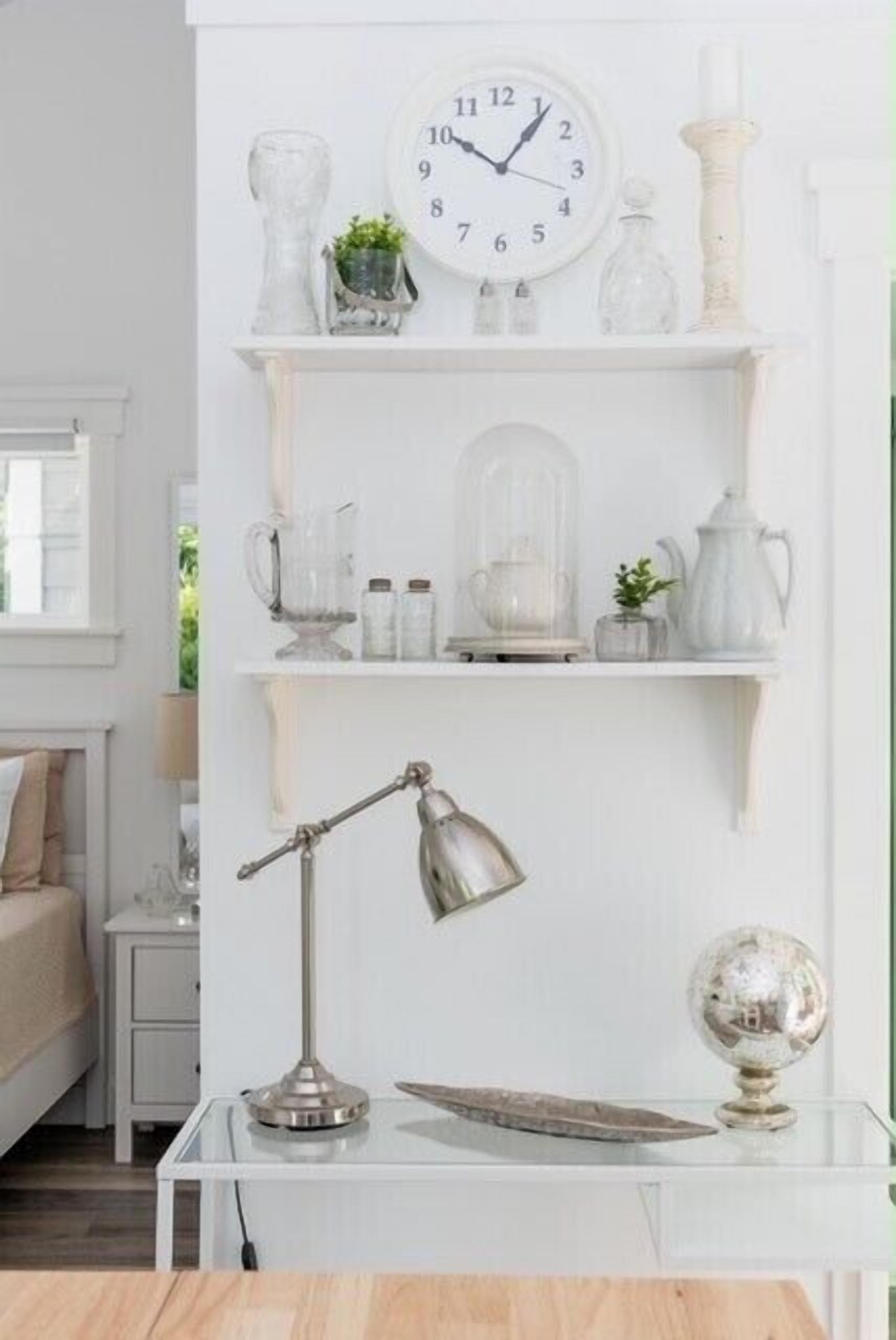 A white room with a clock, shelves with glassware, a desk lamp, and a globe.