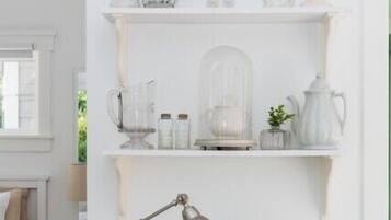 A white room with a clock, shelves with glassware, a desk lamp, and a globe.