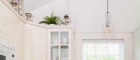 A kitchen with white cabinetry, a window, and a hanging light fixture.