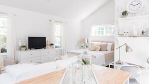 Une chambre à coucher moderne, décorée dans des tons de blanc, avec un lit, une table de chevet et un téléviseur.