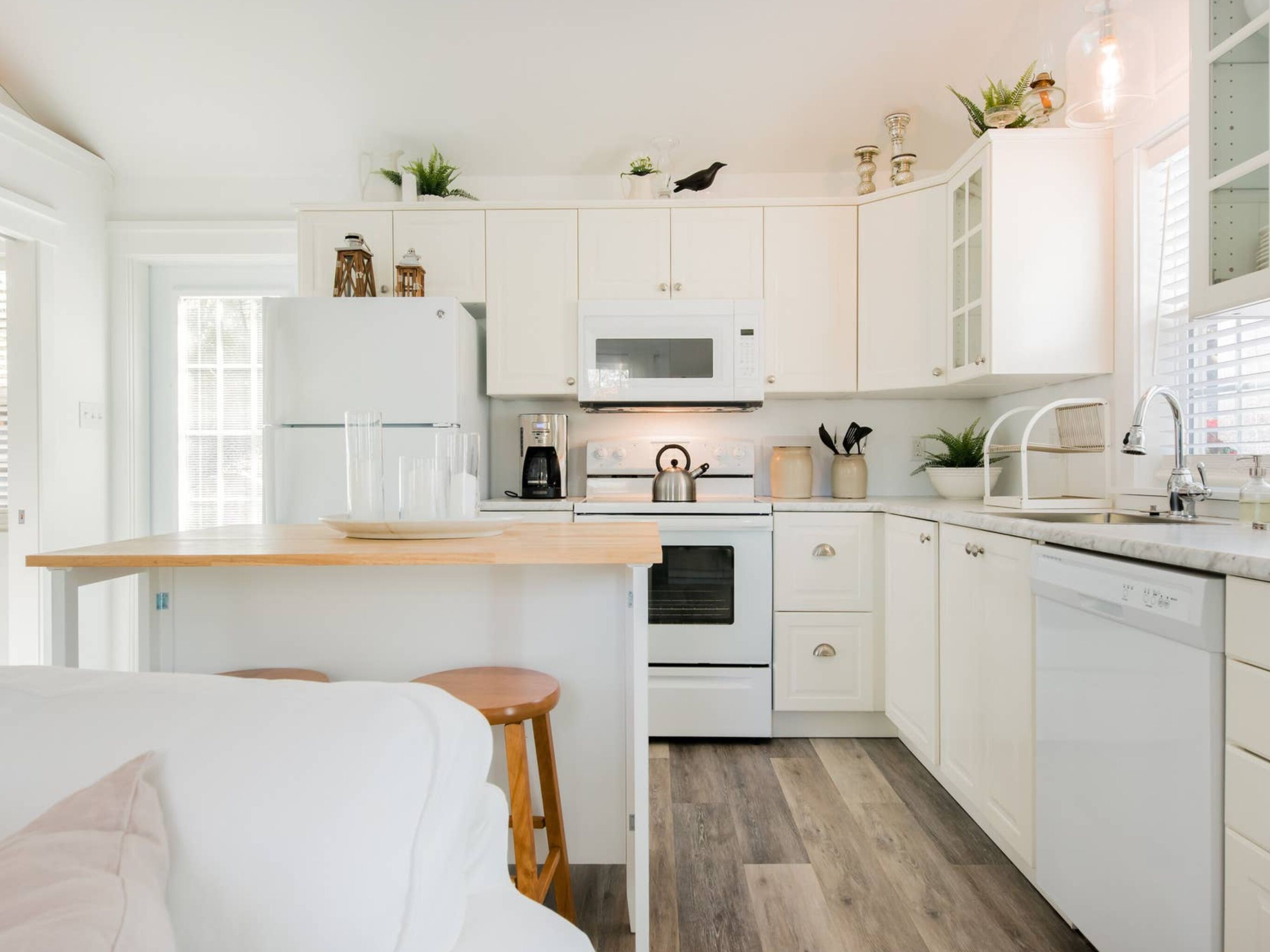 A modern kitchen with white cabinetry, a wooden countertop, and a built-in oven. There are bar stools and a coffee machine.