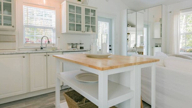 Une cuisine moderne avec des meubles blancs, un plan de travail en bois et un grand miroir.