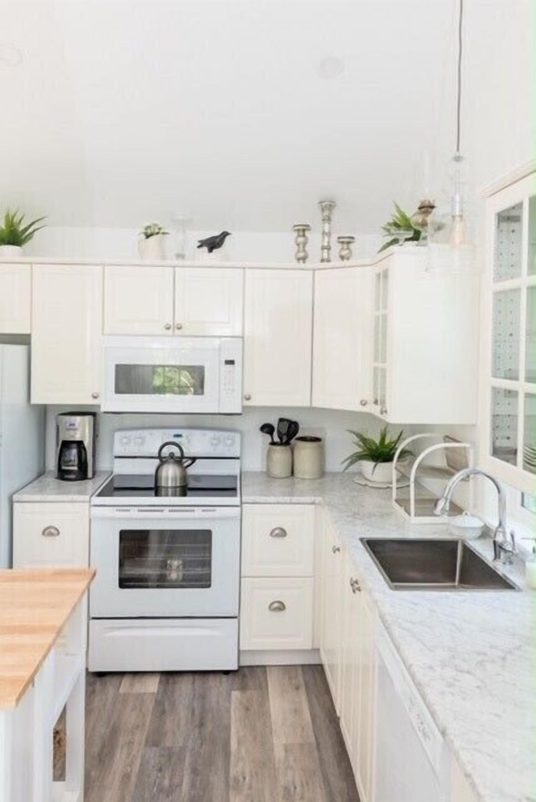 A compact kitchen with white cabinets, a microwave, stove, and a sink.