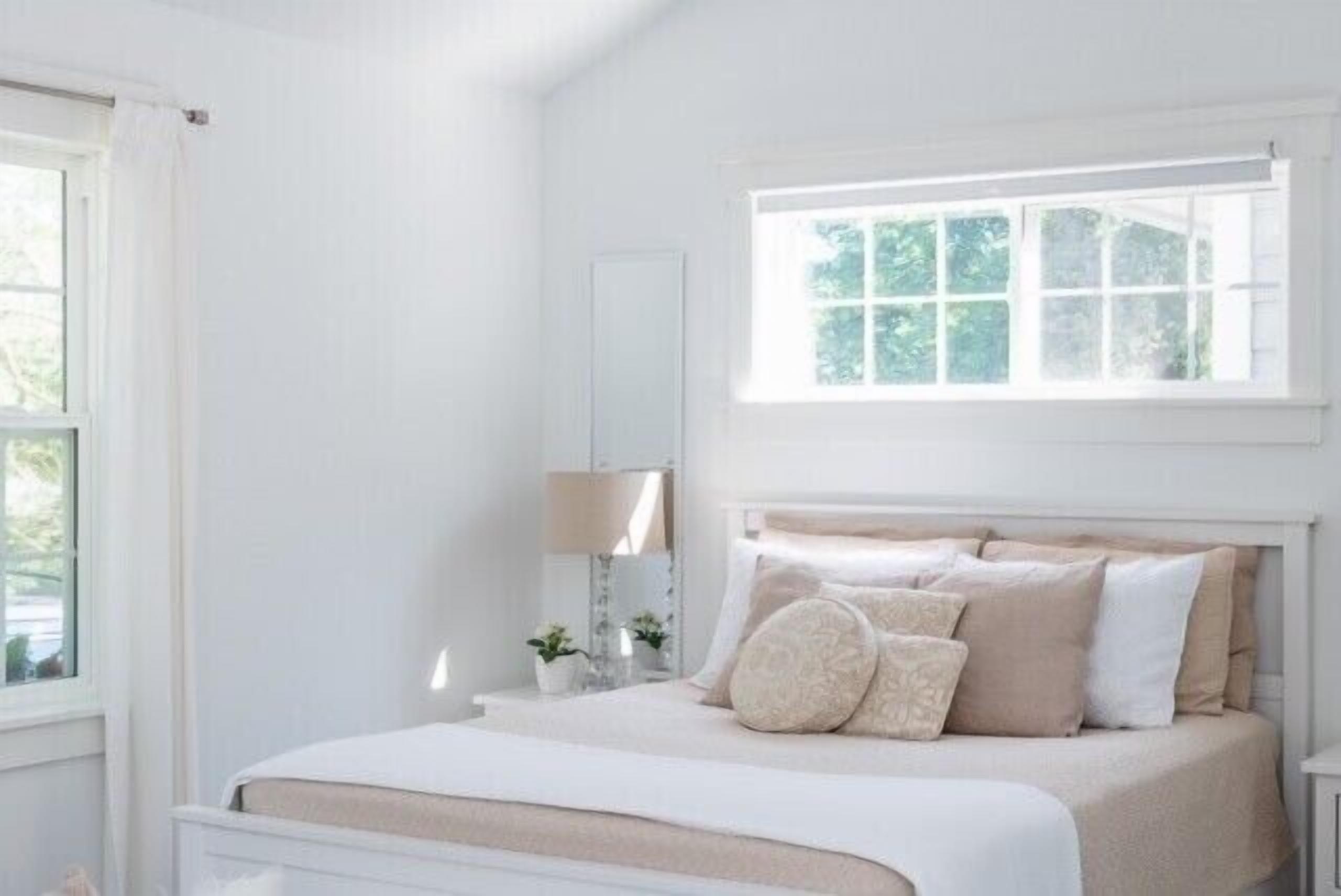 Un dormitorio con cama, ventana y mesita de noche con lámpara.