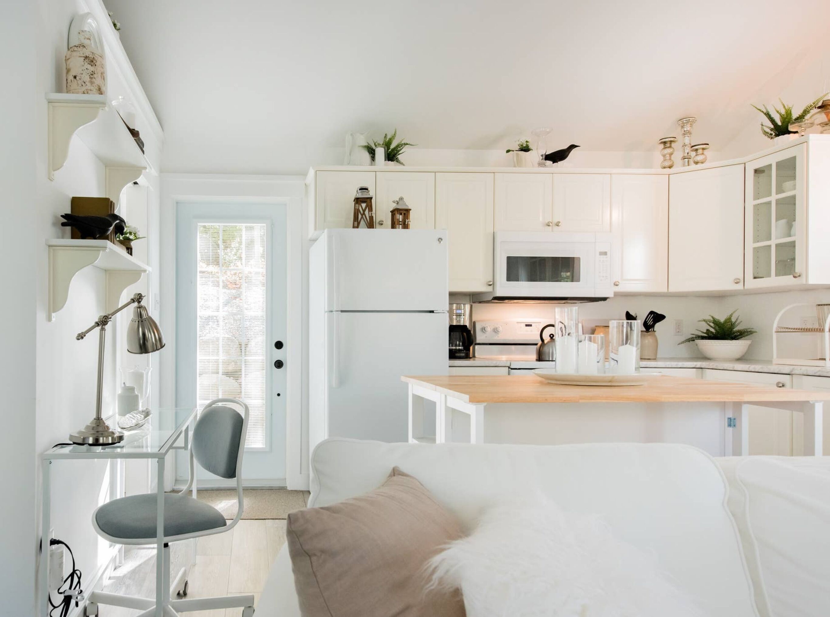 A modern kitchen with white cabinets, a microwave, and a refrigerator. There is a dining table with chairs and a small island.