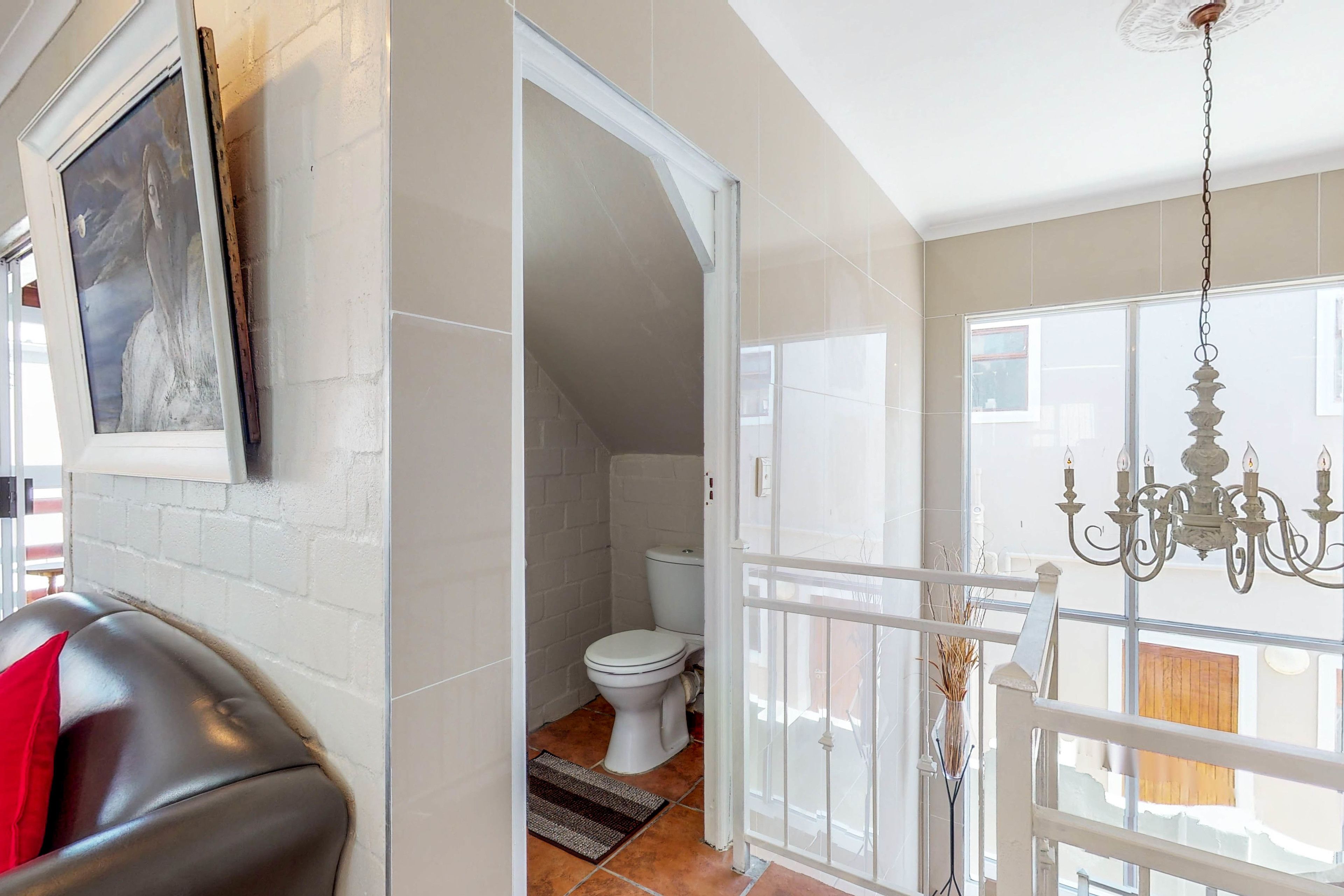 A bathroom with a white toilet, a shower area, and a white door leading to a balcony.