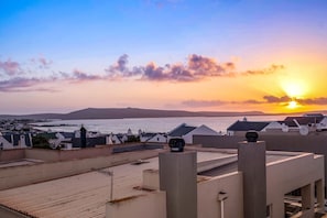 A rooftop terrace with a view of the sea and distant hills during sunset.