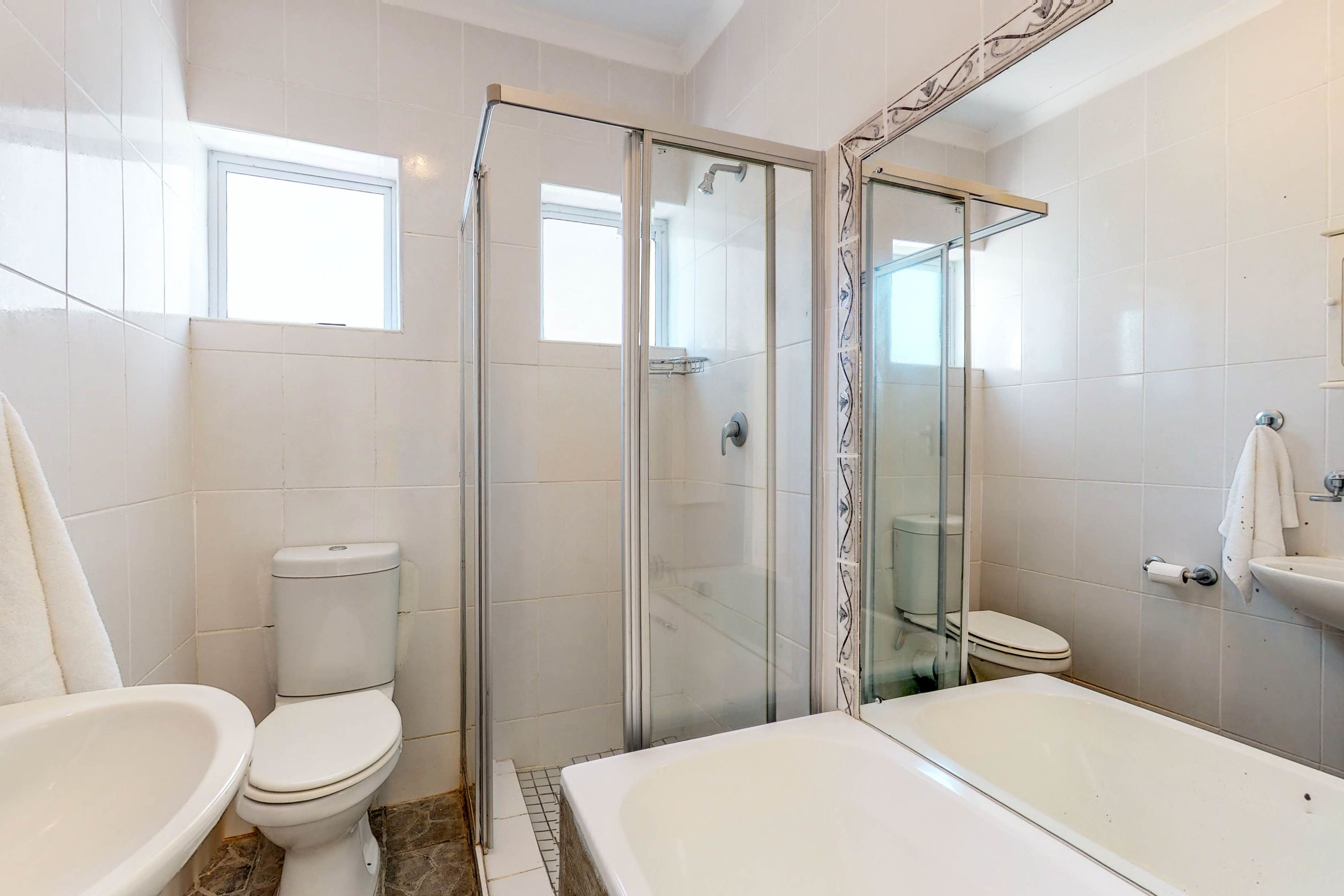 Un baño moderno con ducha envuelta en vidrio, inodoro blanco, bañera y lavabo.