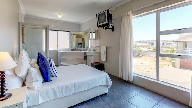 Een hotelkamer met een bed, een aan de muur bevestigde televisie, een badkamer met een spiegel en een groot raam met uitzicht.
