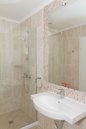 Un baño con ducha envuelta en vidrio, un lavamanos blanco y pared de azulejos.