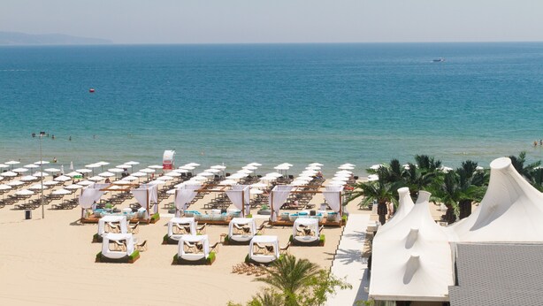 A beachside hotel with rows of sun loungers and umbrellas, a pool area, and a view of the sea. - Europe Hotel & Casino (Sunny Beach)