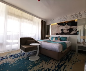 Una habitación de hotel con una cama, una silla, una mesita y un cuadro en la pared.