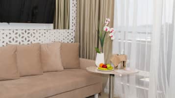 Ein Wohnzimmer mit einem beigen Sofa, einem kleinen runden Tisch mit Blumenvase, Obstschale und einer Lampe.