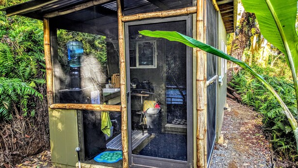 A small, bamboo-framed structure with a sliding glass door, a small porch area, and a visible kitchen inside.