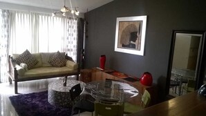 Ein Wohnzimmer mit einer Couch, einem runden Glastisch und einem Essbereich mit Stühlen.