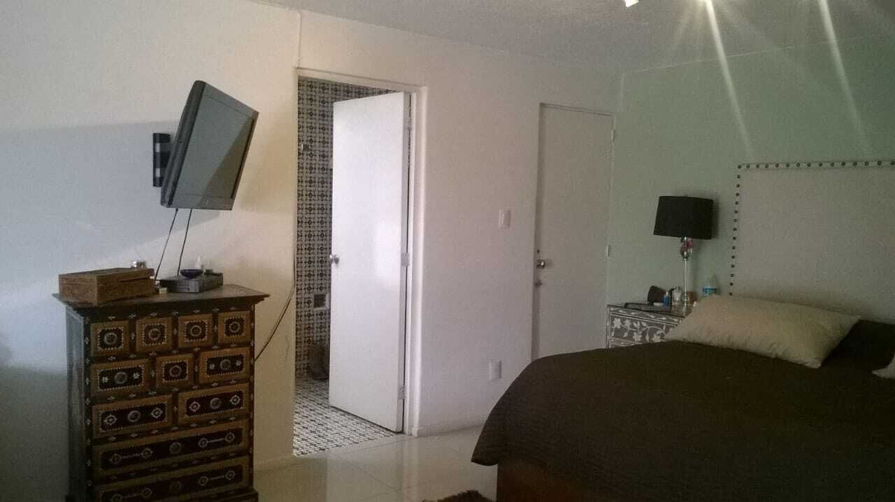Ein Schlafzimmer mit einem Bett, einem Schminktisch, einem Fernseher und einer Tür zu einem weiteren Raum.