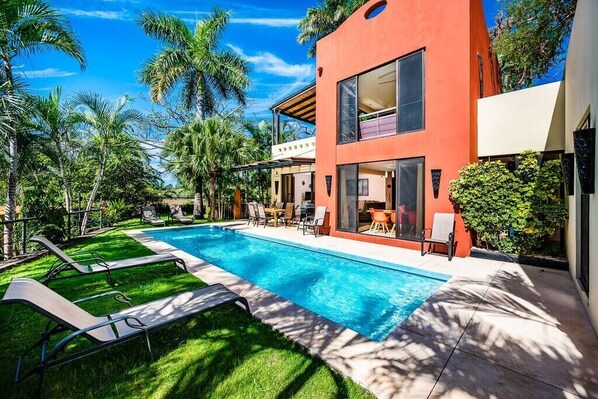 Une maison moderne dotée d’une piscine, entourée d’une végétation luxuriante et de palmiers.