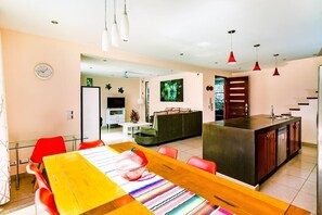 Une cuisine moderne dotée d’un îlot central, un coin repas avec une table en bois et des chaises rouges, et un espace de détente avec un canapé et un téléviseur.