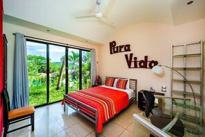 Une chambre avec un grand lit, un bureau, une chaise et une vue sur la verdure.