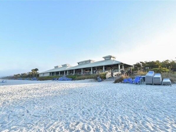 A beachfront property with a large building, outdoor seating, and a sandy beach.