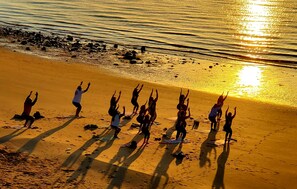A group of people performing yoga on mats on a beach with the sun setting in the background.