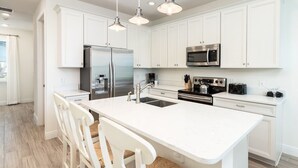 A modern kitchen with white cabinetry, stainless steel appliances, and pendant lighting.