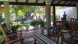 A covered patio with wooden furniture, a pool, and lush greenery. - Green wood villa (Negombo)