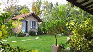 A brick house with a tiled roof, surrounded by a well-maintained garden with various plants and a small tree in a planter. - Green wood villa (Negombo)
