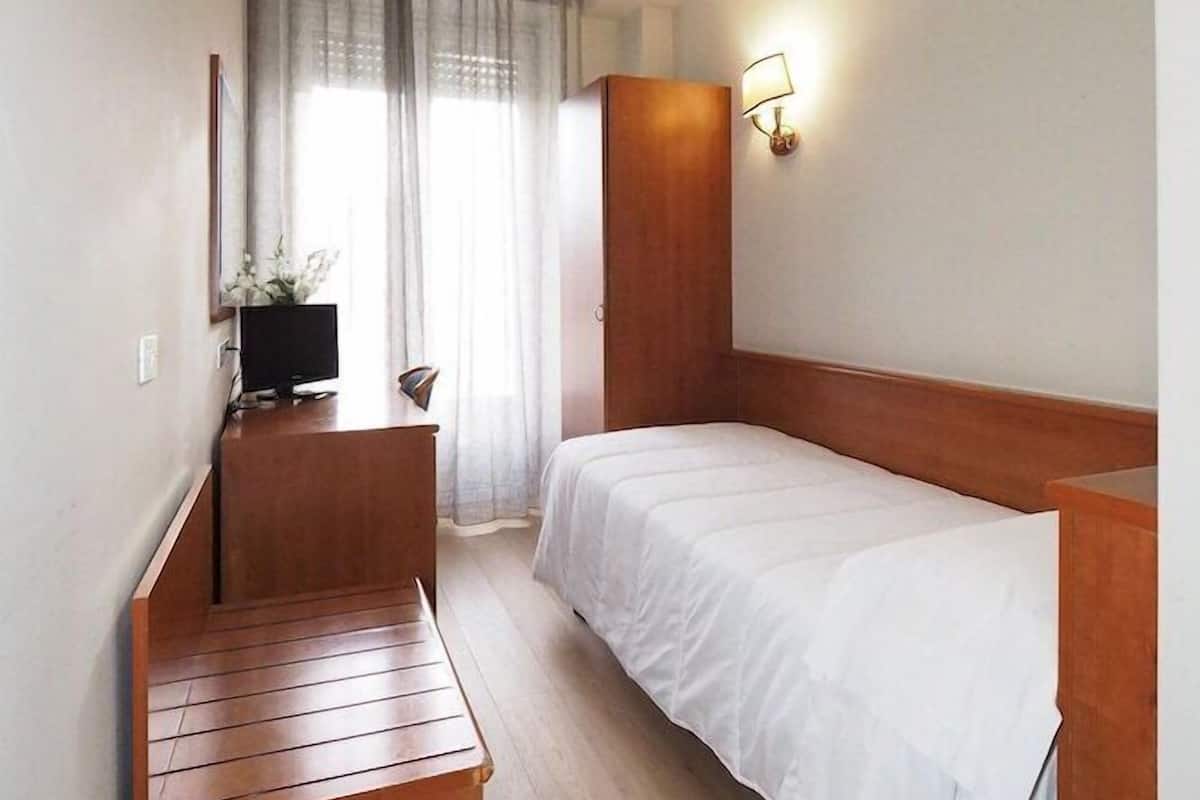 Une chambre d’hôtel avec un lit, un banc en bois, une télévision et une fenêtre avec des rideaux.