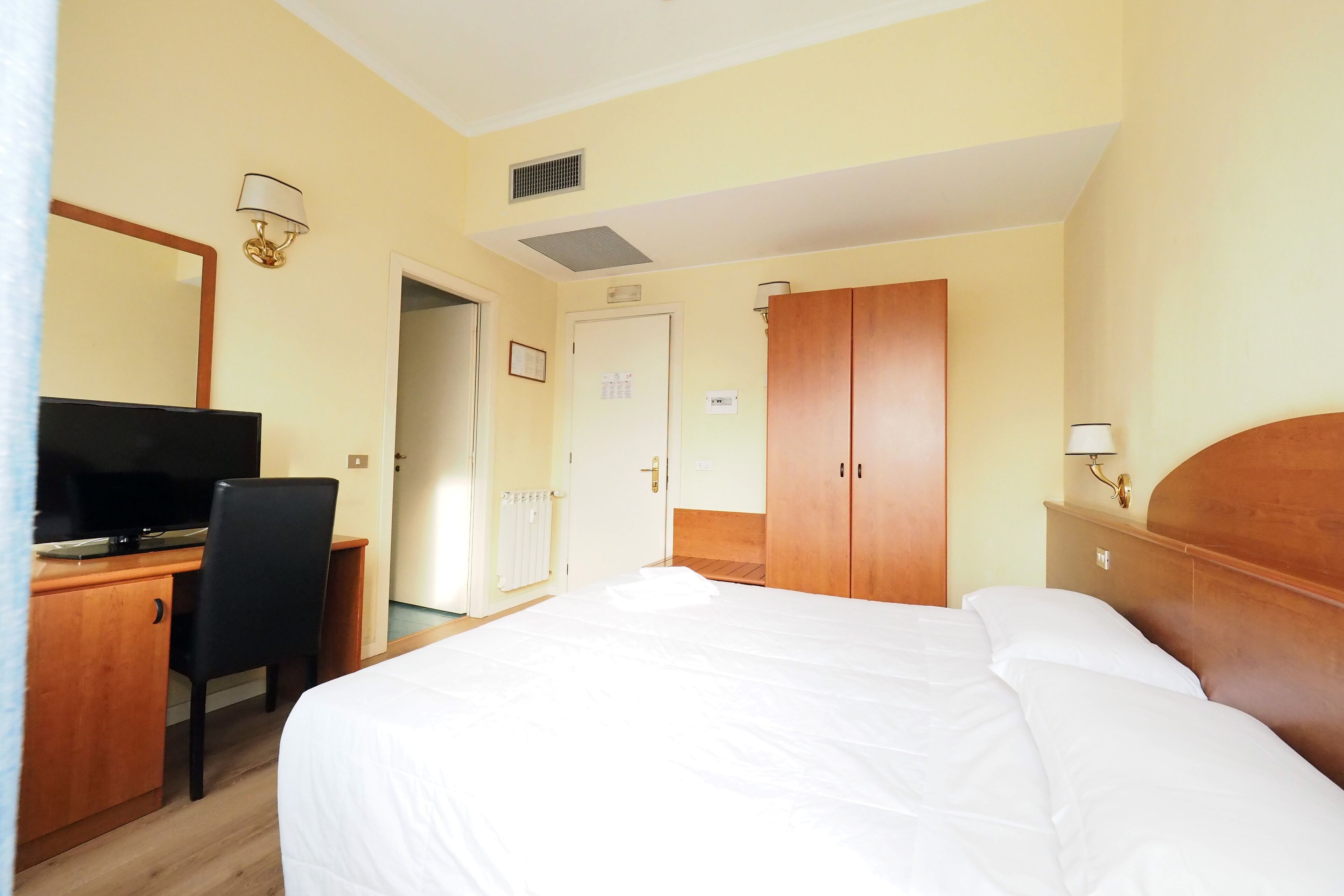 Una habitación de hotel con cama, escritorio, silla, televisor, armario y lámpara.