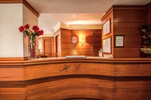 A reception desk with a wooden finish, a vase of red roses, and a sign indicating a no-visitor policy. - Hotel Laura (Rome)