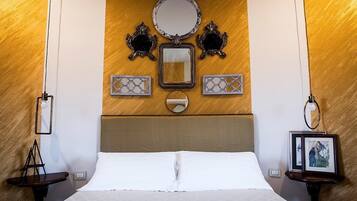 Habitación de hotel con una cama grande, cabecera de madera, espejo redondo, dos apliques de pared y una mesita de noche con un marco de fotos.