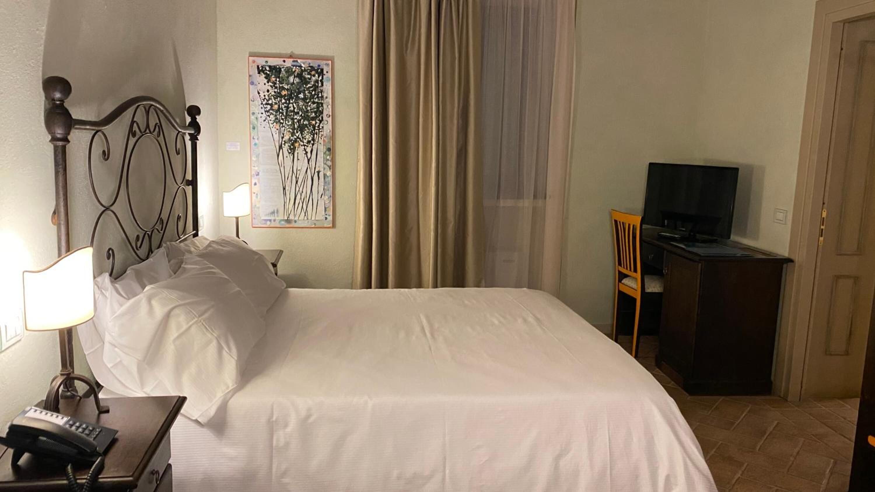 A hotel room with a bed, a desk with a television, a lamp, and a telephone.