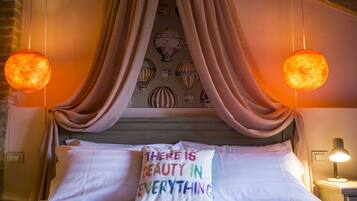 Una cama con sábanas blancas, un almohadón con texto de colores y un dosel.