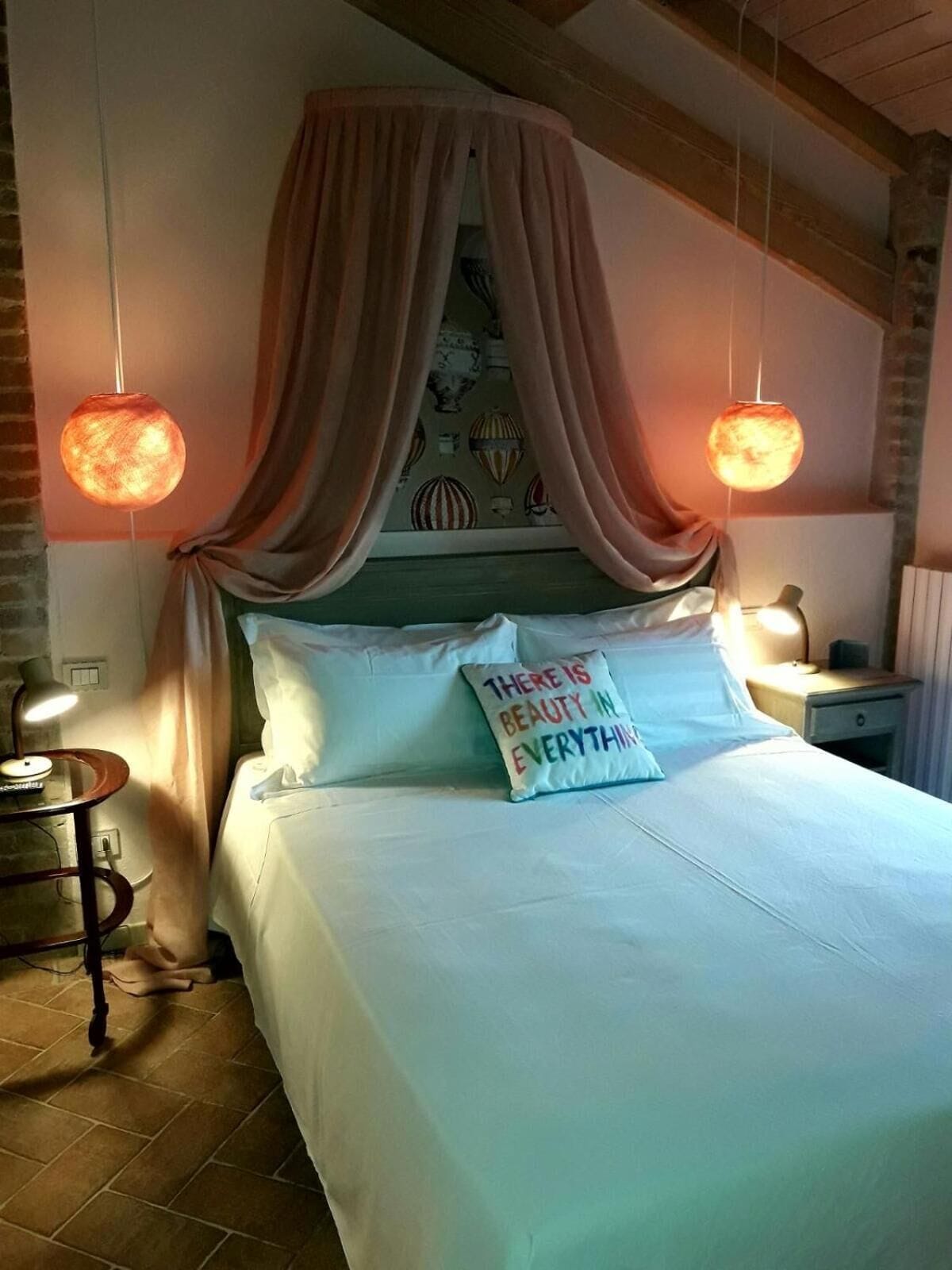 A bedroom with a canopy bed, two bedside lamps, a nightstand, and a decorative pillow.