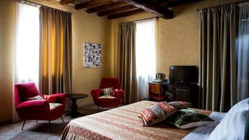 Una camera d'albergo con un letto grande, due poltrone rosse, un tavolino, una televisione e un quadro appeso al muro.