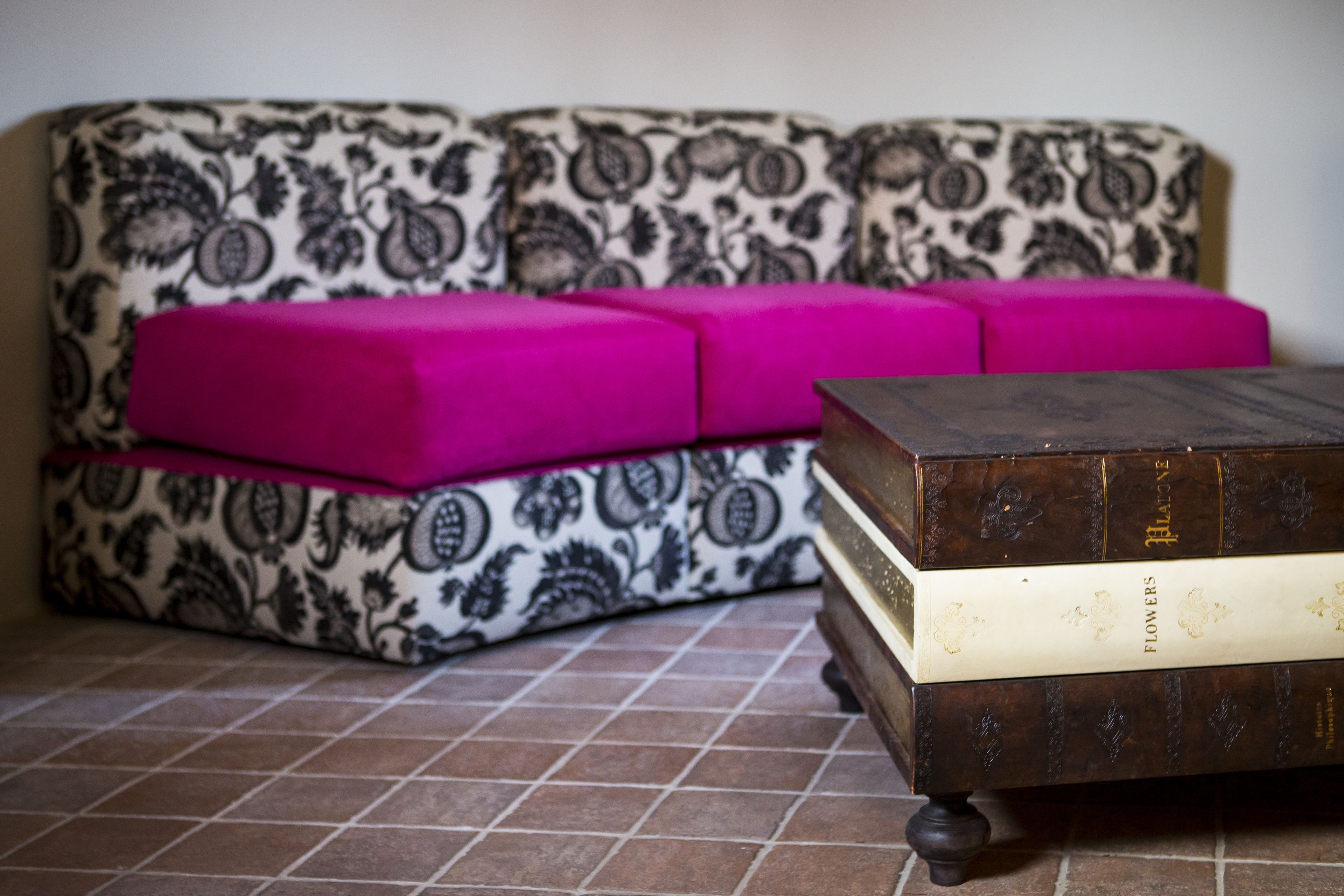 A patterned sofa with a pink cushion, a wooden side table, and a stack of books.