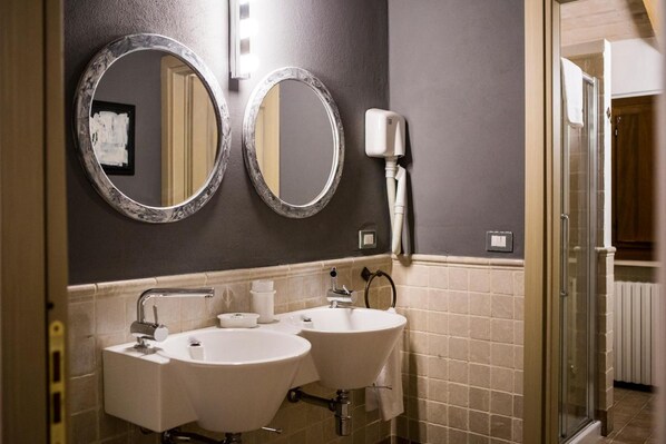 A bathroom with two sinks, a mirror, a towel dispenser, and a shower. - Relais Cascina Scottina (Cadeo)
