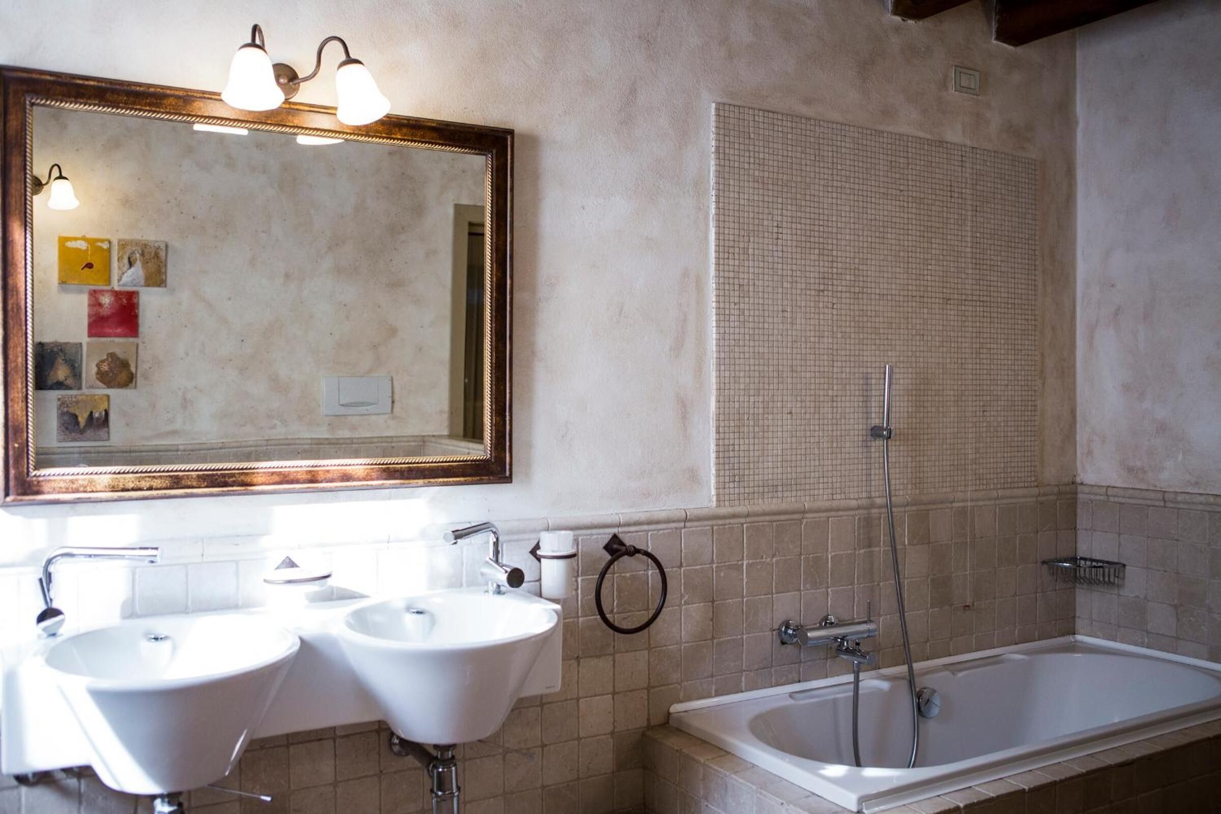 Un baño con dos lavamanos, una bañera y un espejo grande con iluminación.