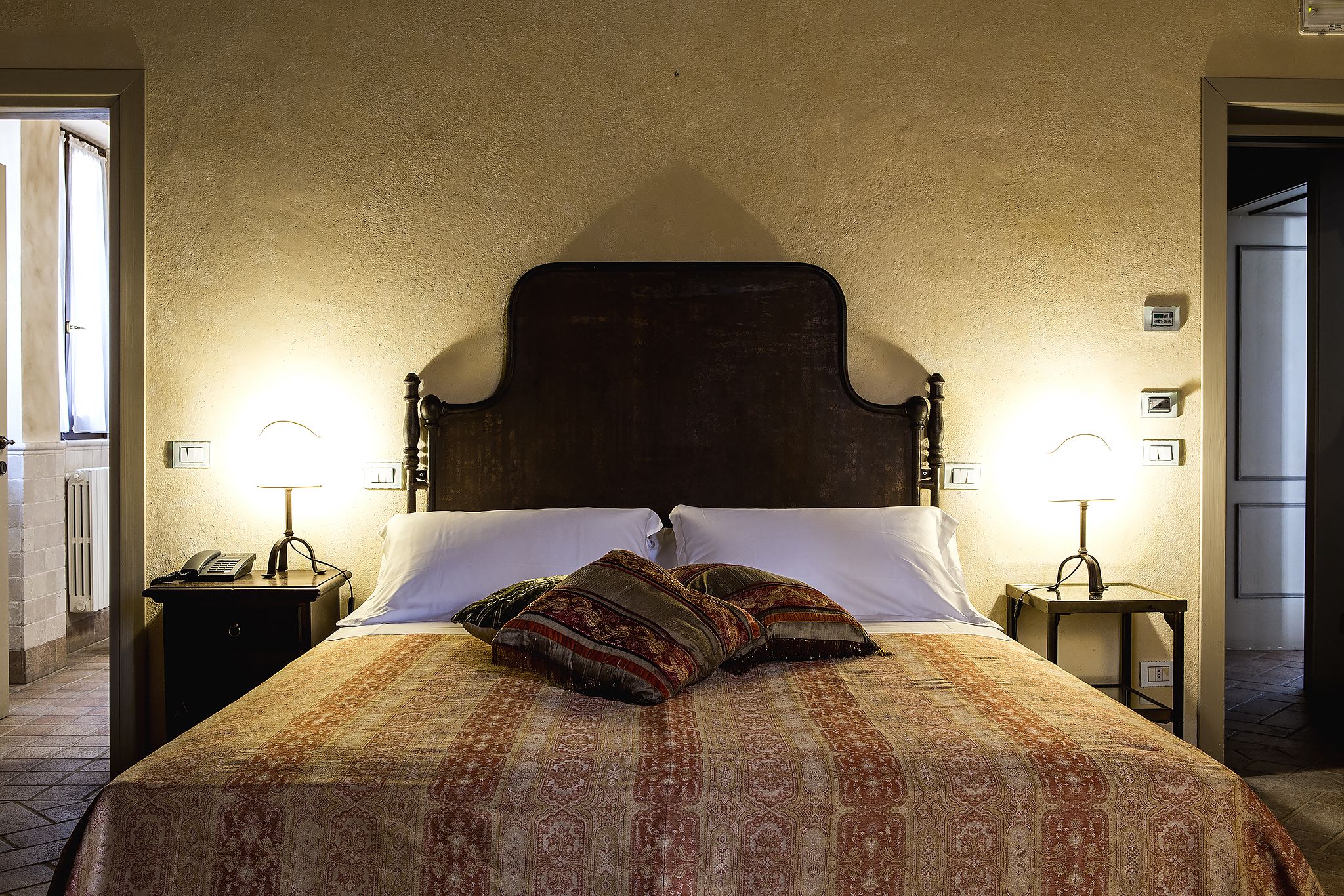 Un letto rifatto con cura, copriletto decorato e due cuscini ornamentali, affiancato da comodini con lampade.