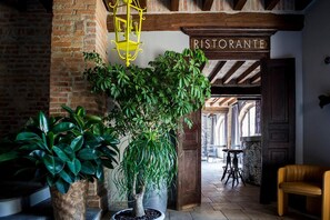 A rustic interior with a brick wall, a large potted tree, a yellow hanging light fixture, and a sign reading "RISTORANTE". - Relais Cascina Scottina (Cadeo)