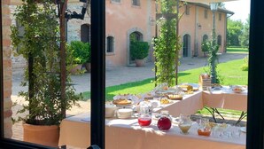 Un espace extérieur aménagé pour les repas, avec des tables dressées, entouré de plantes en pot et d’un bâtiment en arrière-plan.
