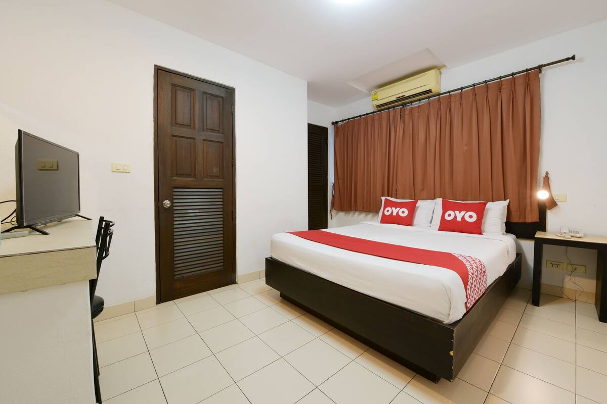 Een hotelkamer met een bed, een bureau, een televisietoestel en een airconditioning.