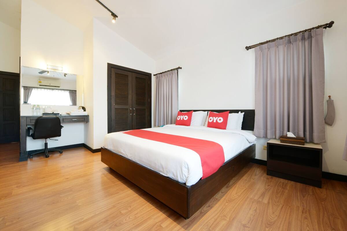 Een slaapkamer met een houten bed, een bureau met stoel, een kledingkast en een nachtkastje met lamp.