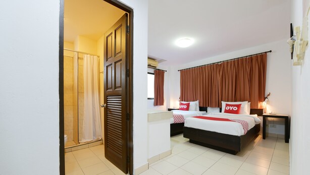 Habitación de hotel con cama, mesita de noche, cortinas en la ventana, puerta y zona de ducha.