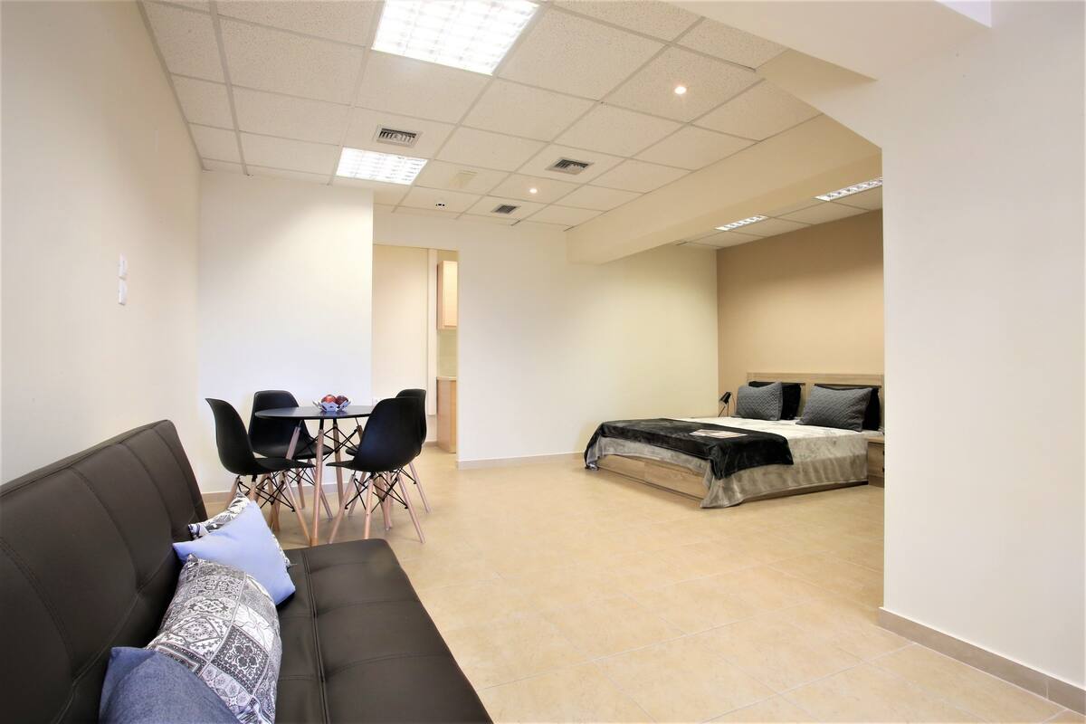 A hotel room with a bed, a sofa, a dining table with chairs, and a kitchenette area.
