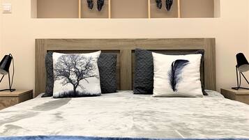 Un dormitorio con una cama grande, dos almohadas con diseños de árboles, una manta azul y dos obras de arte con plumas enmarcadas en la pared.
