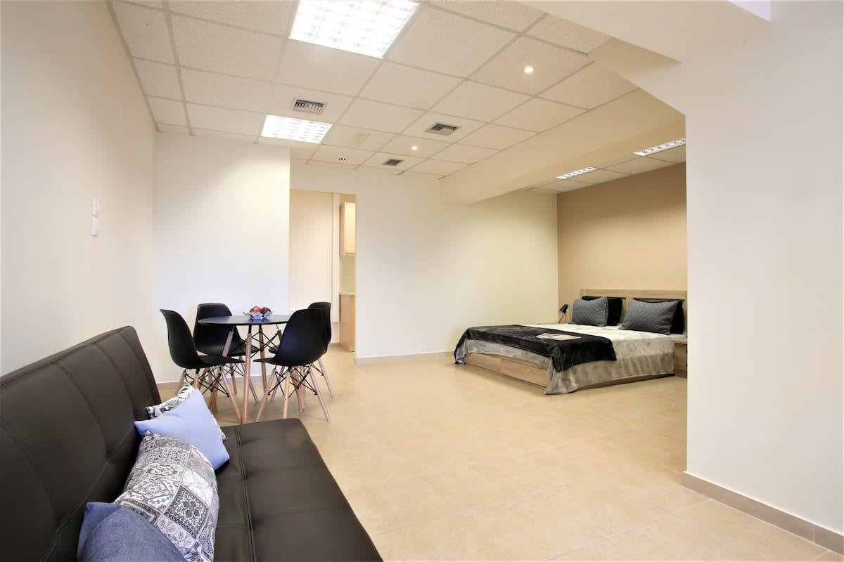 A hotel room with a bed, a sofa, a dining table with chairs, and a kitchenette area.