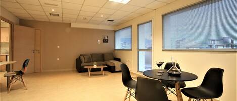 A modern room with a round table, black chairs, a sofa, and large windows with blinds.